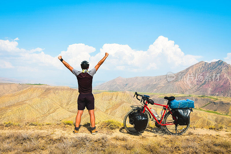 近距离后景，鼓舞人心，兴奋，快乐的高加索男性骑着红色的旅游自行车在荒凉的山区，举手自信，无忧无虑的生活方式