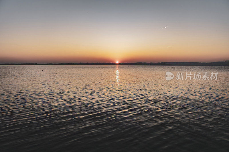 意大利加尔达湖上美丽的日落，太阳反射在平静的水面上
