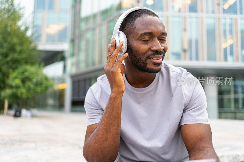 音乐歌曲概念。好的开始。快乐的非裔美国人在城市街头听着现代音乐。戴着耳机的人喜欢在户外听自己喜欢的音乐。人们的生活方式快乐。