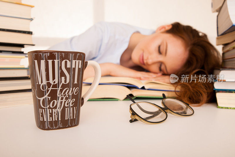 漂亮又疲倦的学生睡在一堆书上，桌上放着一个咖啡杯