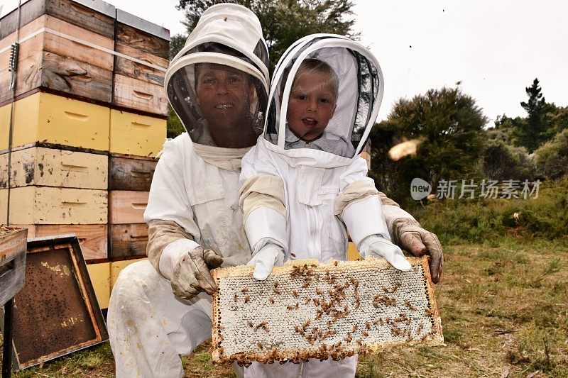 孩子在蜜蜂套装拿蜂蜜框架与导师