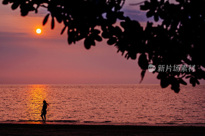 在日落海滩上漫步的年轻女士的剪影