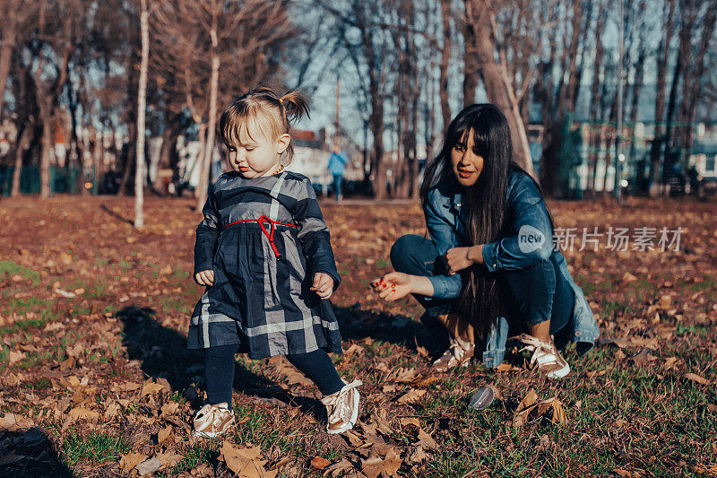 年轻的母亲和她蹒跚学步的女儿在公园里玩耍