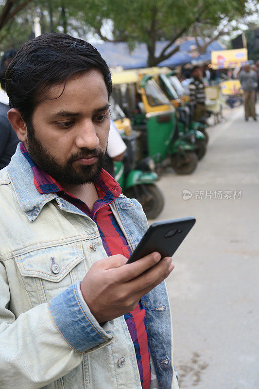 印度男子看手机屏幕看短信，拿着手机查看社交媒体，浏览智能手机设备技术的新信息，三轮车在印度交通