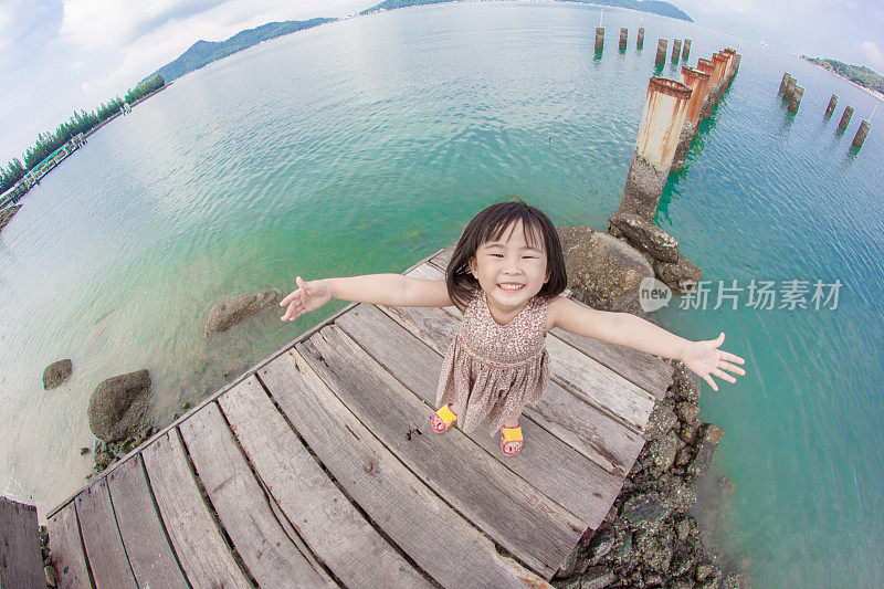 在一个阳光明媚的公园里，一个小女孩在海滩边微笑着摆姿势拍照