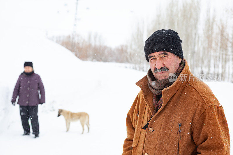 一对老年夫妇在下雪的乡村路上穿着暖和的衣服