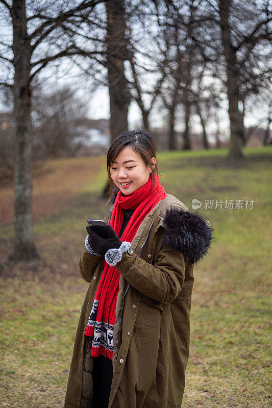 年轻的亚洲女性在温暖的冬天使用智能手机