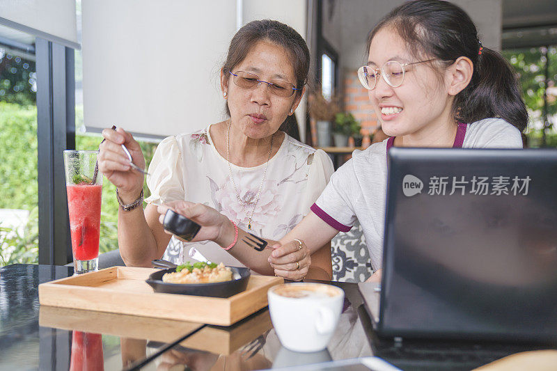 亚洲家庭年轻的青少年和母亲在度假吃甜点和喝果汁，使用数字平板电脑和智能手机在咖啡馆