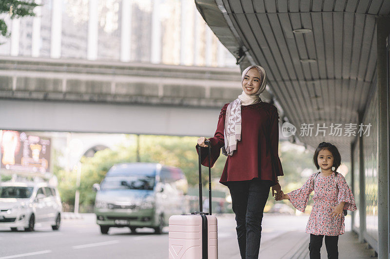 年轻的亚洲马来人母亲和女儿提着行李走在街上