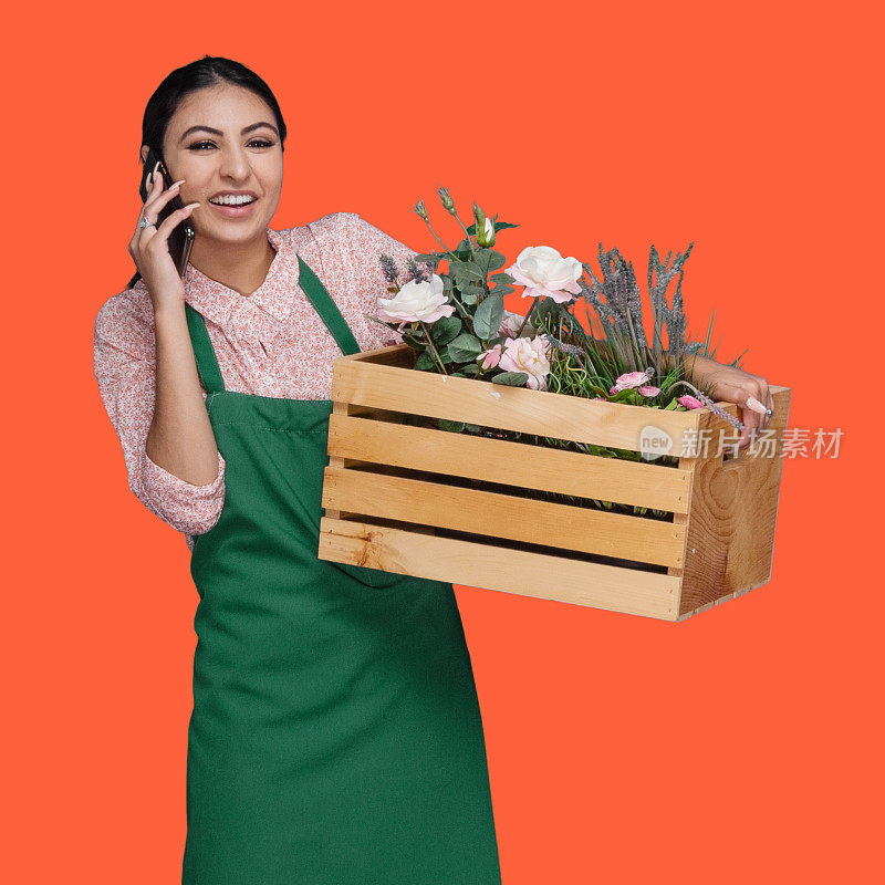 拉丁美洲和西班牙裔的年轻女性业主前面的橙色背景穿着衬衫，手持植物和使用手机