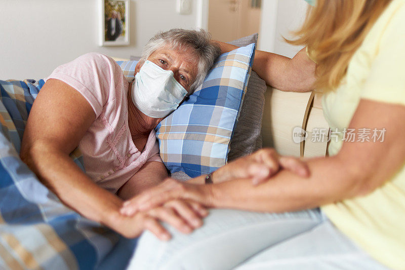 一个女儿和感染Covid-19病毒的母亲坐在床上，两人都戴着呼吸口罩或防护口罩