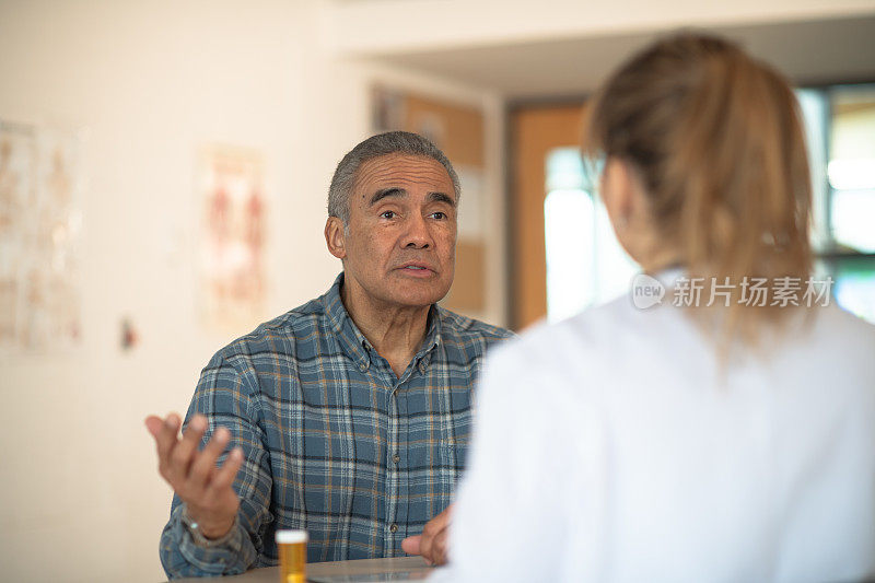 老年男性有色病人讨论他的疼痛在医疗咨询