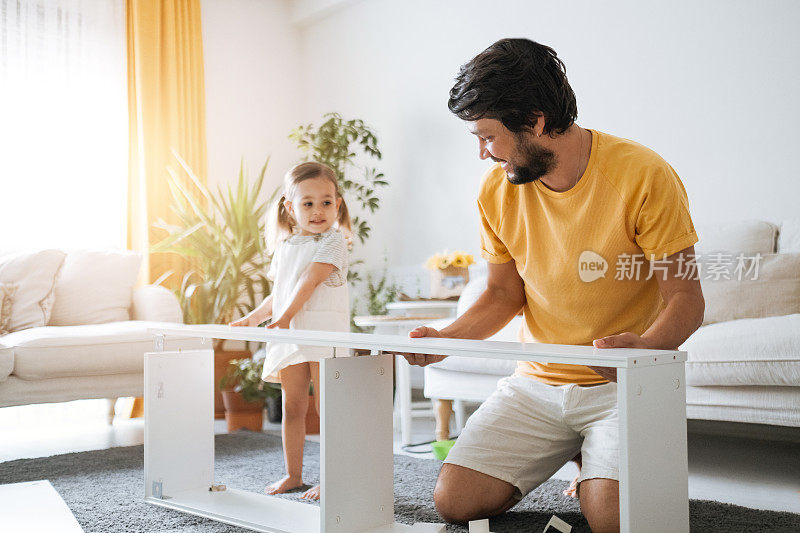 在他们的起居室里，小女孩在他父亲的帮助下试图组装家具