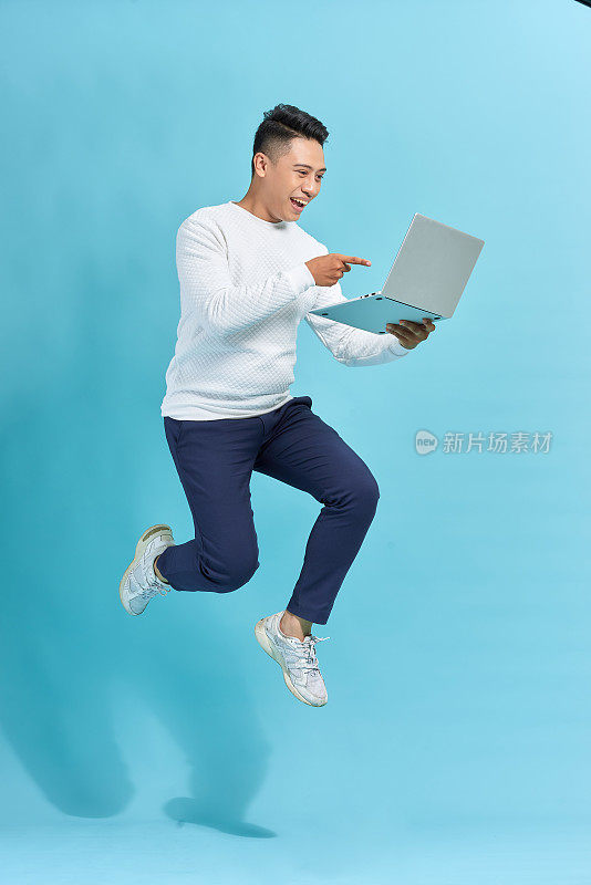 有魅力的成功人士用笔记本电脑在空中跳来跳去，居家工作，孤立在蓝色背景下