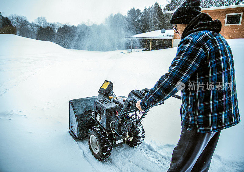 老人正在用吹雪机清理积雪。