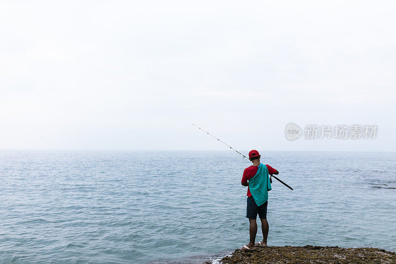 亚洲男子戴着帽子在海滩上钓鱼