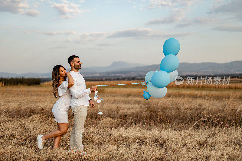 年轻的孕妇和年轻的男子在大自然中拿着蓝气球