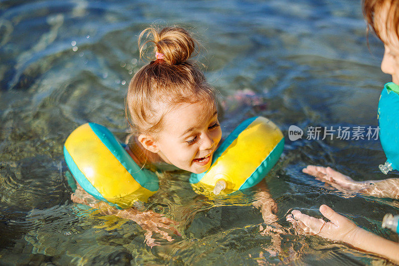 快乐的笑着蹒跚学步的女孩与朋友在海里玩得开心