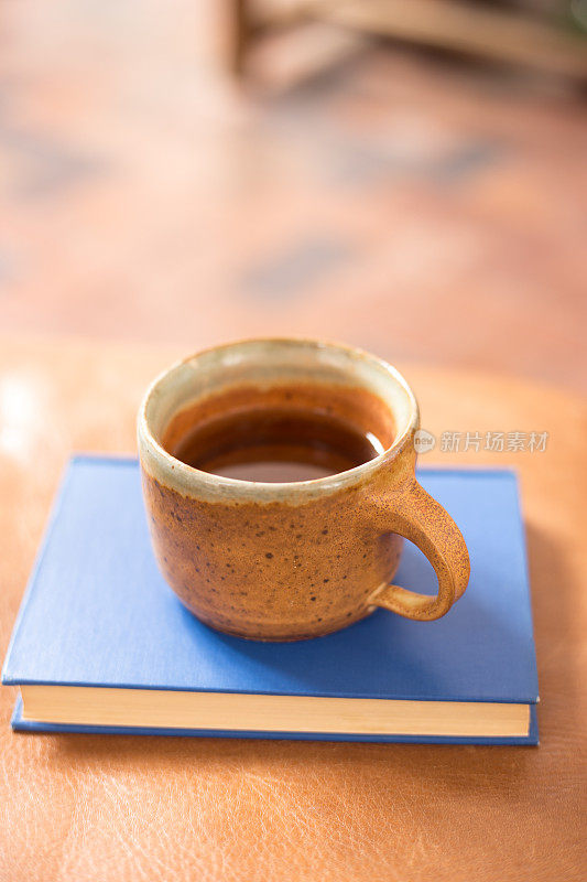 茶杯上的蓝色书在皮革脚凳上