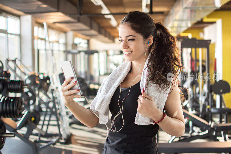 在健身房戴着耳机使用智能手机的运动型女性。