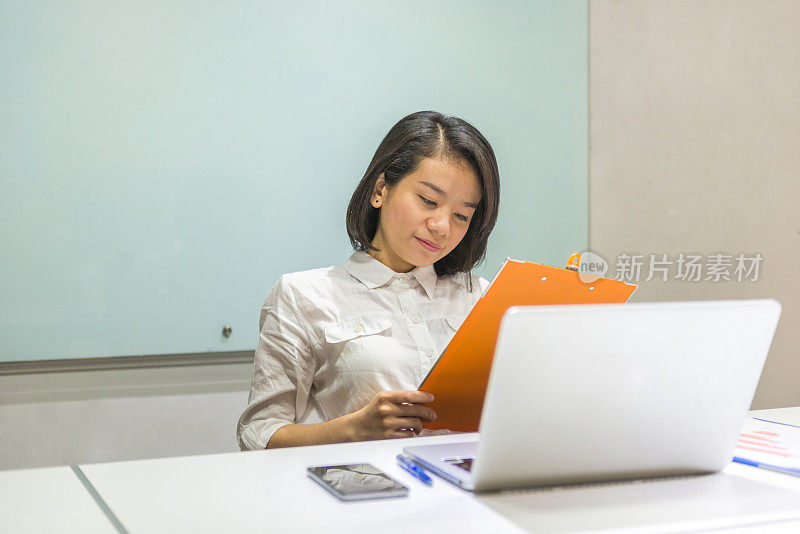 女经理阅读报告并使用笔记本电脑工作