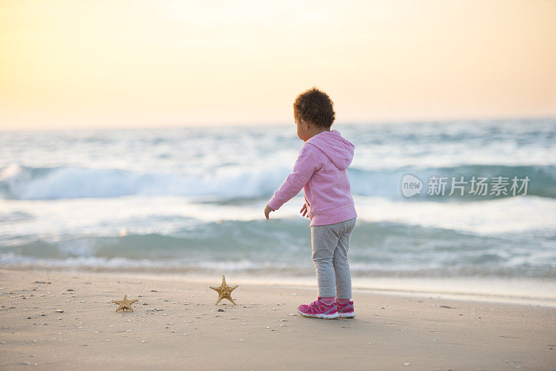 蹒跚学步的小女孩在海滩上玩海星。