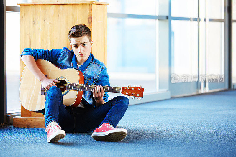 酷少年拿着吉他坐在走廊的地毯上