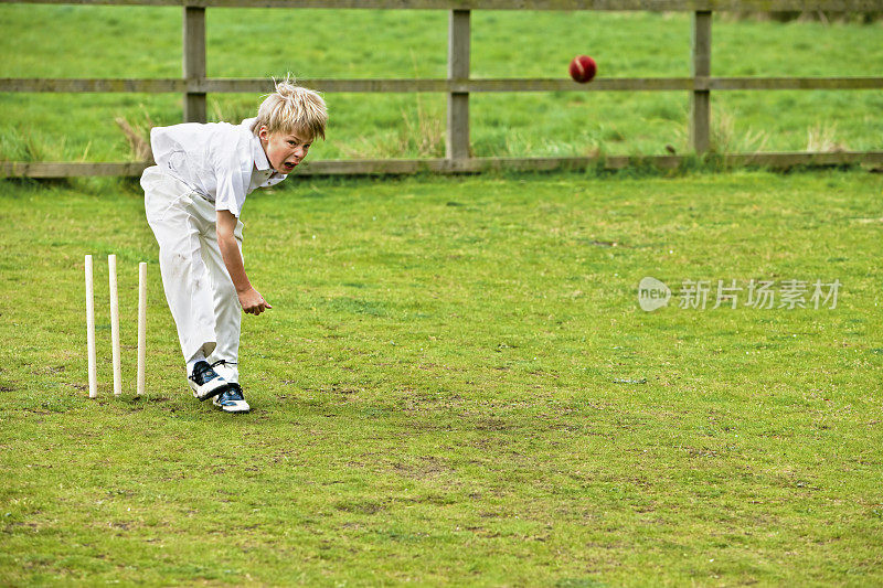 男孩打板球与保龄球行动在草地上