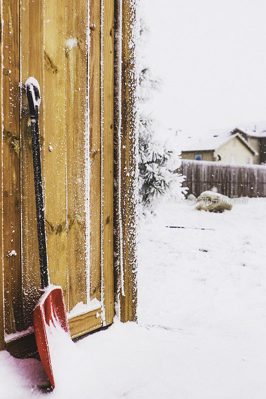 雪铲抵在雪棚上的木棚。住宅的背景。