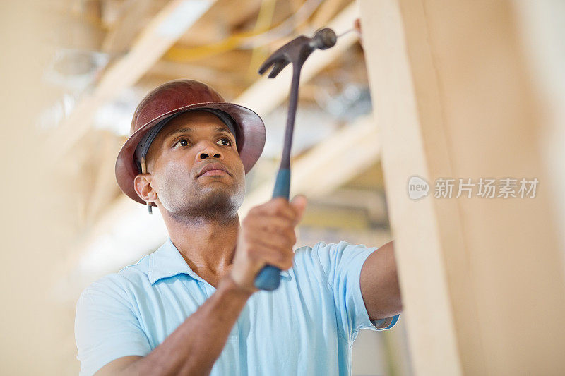 一名男性建筑工人正在工地上把钉子钉进木头里