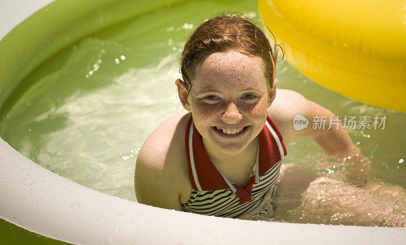 雀斑脸红发女孩微笑，孩子在塑料游泳池