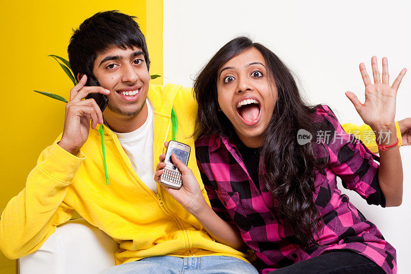 两个年轻的印度成年人坐在沙发沙发上，拿着手机