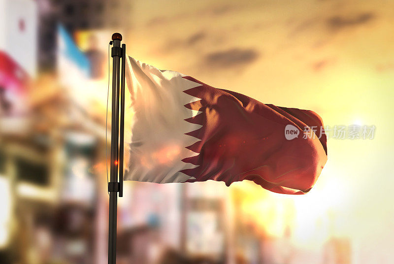 在日出的背光下，卡塔尔国旗映衬着城市模糊的背景