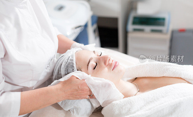 用无菌餐巾纸擦拭面部。年轻漂亮的女人正在美容院接受治疗。洁面泡沫使用。