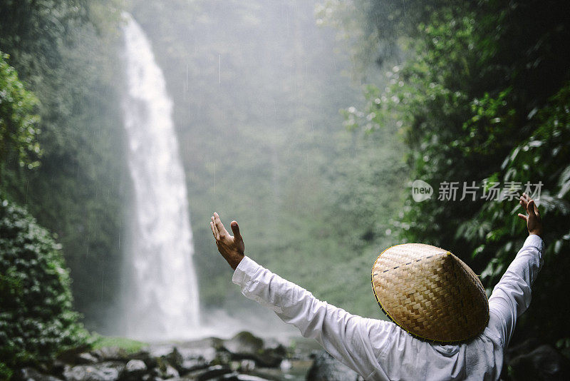 在瀑布旁举手祈祷的亚洲人