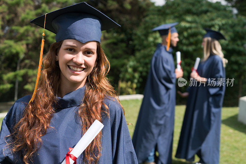 骄傲的女高中毕业生拿着她的文凭，看着镜头微笑