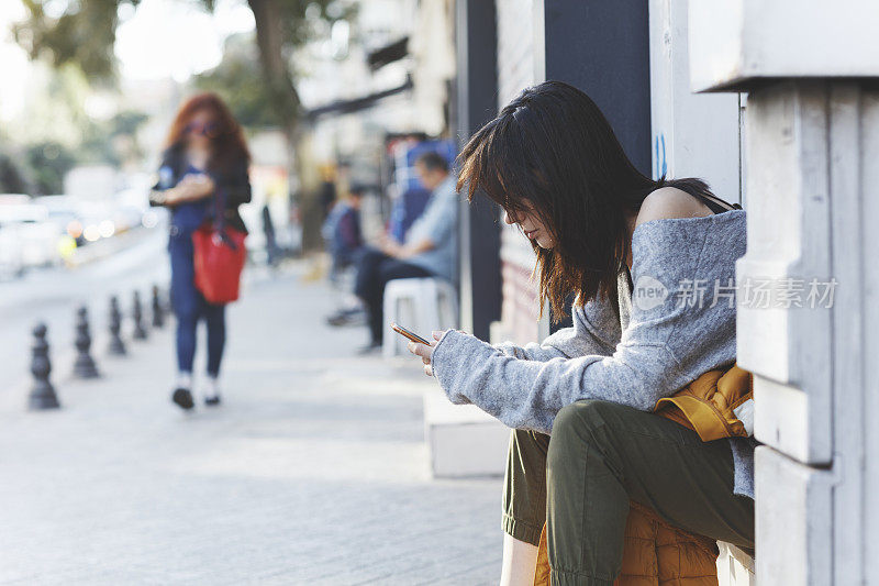 年轻女子坐在靠近临街门的地方，使用智能手机