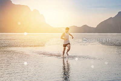 年轻的亚洲男子在海滩上奔跑，夕阳为背景