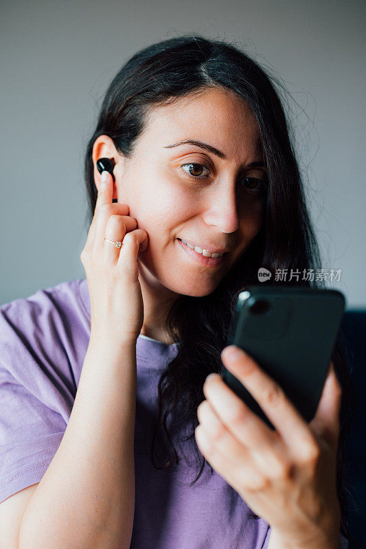 女人戴着无线耳机，拿着智能手机