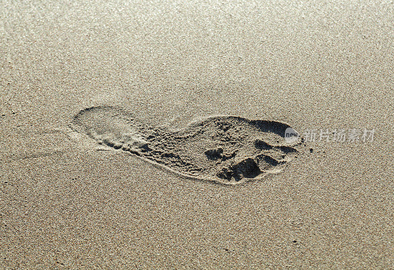 一个人赤脚的右脚脚印在棕黄色的沙滩背景