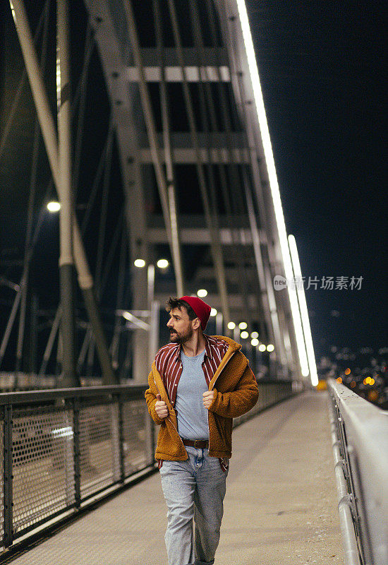 年轻时髦的男人晚上走在桥上