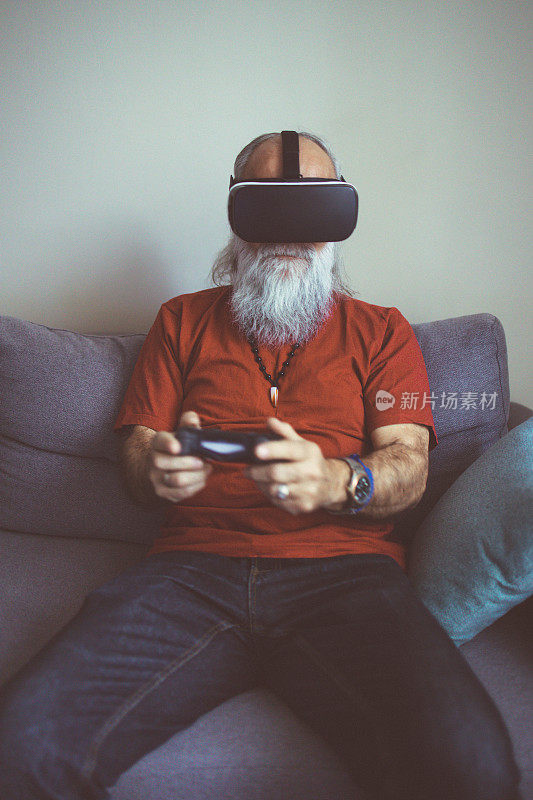 一名大胡子老人在家用VR和手柄玩视频游戏。