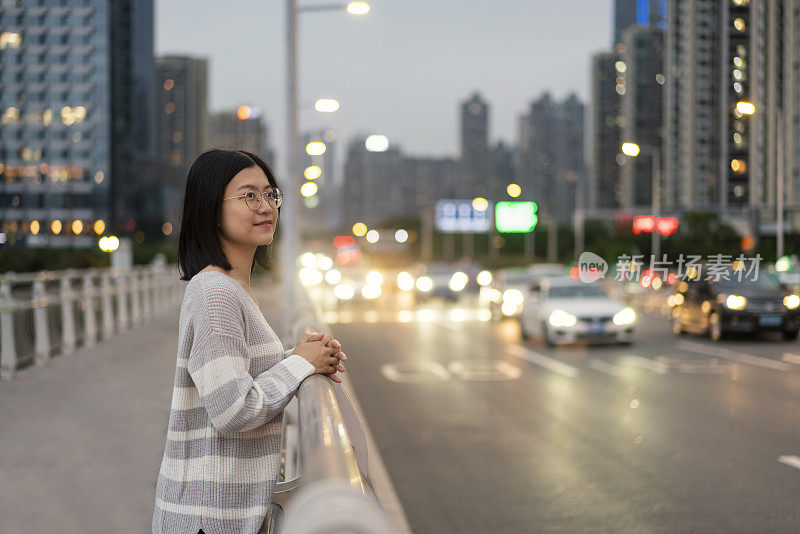 在市中心的一座桥上，一位亚洲妇女望着远方