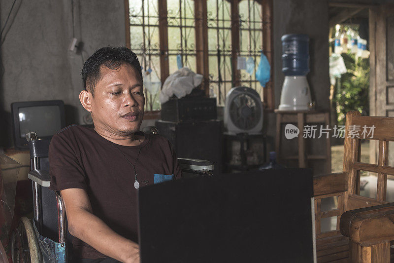 一个残疾人在他的笔记本电脑上审查他的任务。一名在其农村家中工作的独立和受雇轮椅使用者。