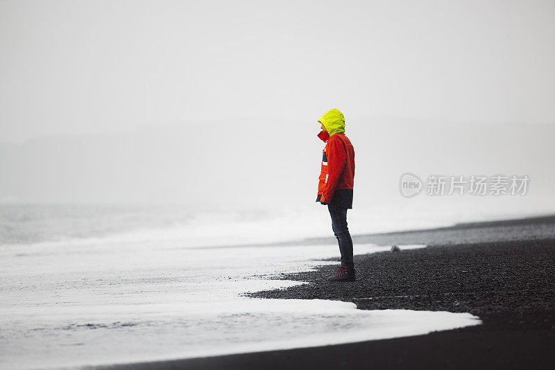 穿着红色夹克的男人站在Reynisfjara海滩上