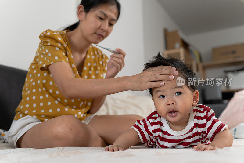 年轻的亚洲母亲照顾和使用数字体温计和手检查体温她的儿子在疾病期间流感发烧。家庭宝宝生活方式照顾和保健理念。