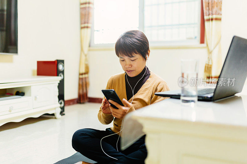 一位中年妇女在瑜伽垫上用手机学习健身之道——科技与生活，健康的生活方式