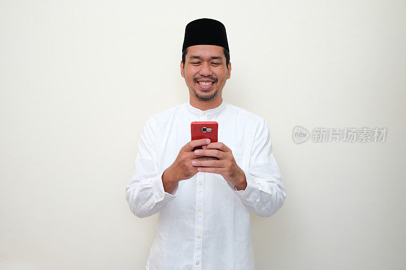 穆斯林亚洲男子笑着用他的手机发短信