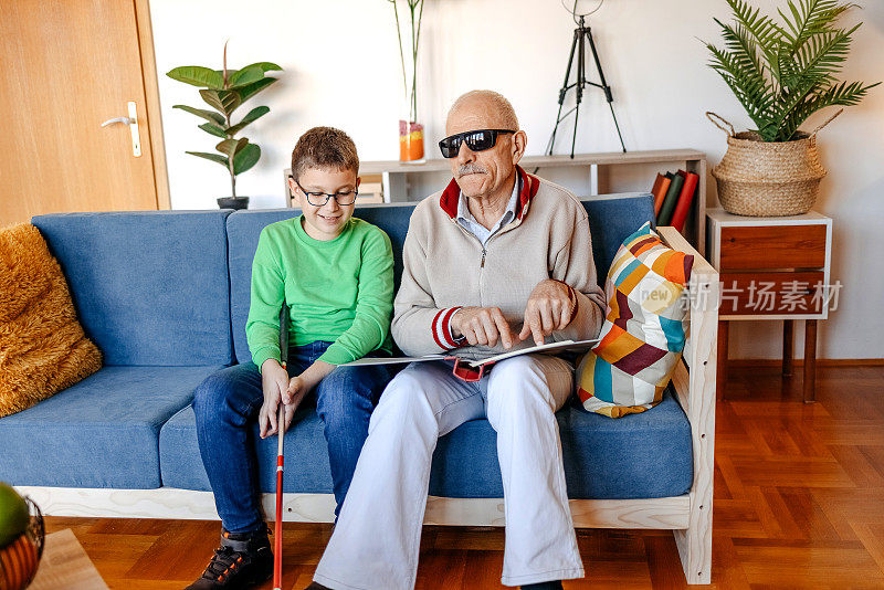 一个盲人老人和孙子坐在客厅的沙发上