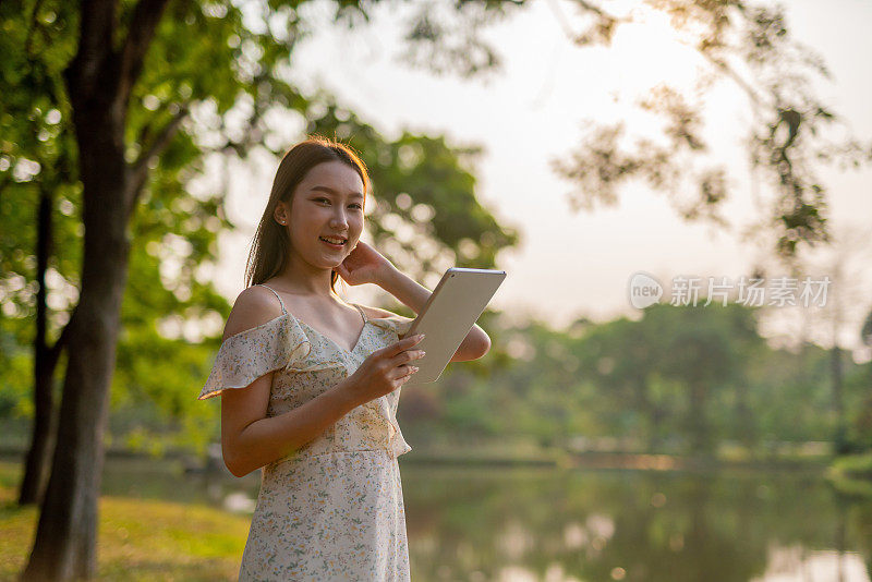 美丽的亚洲女人在公园里玩她的数码平板电脑。在户外工作的年轻女性，一个数字游民